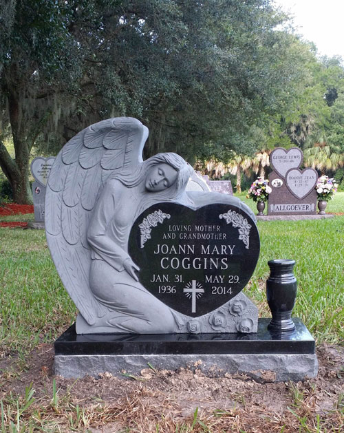 A carved sleeping angel resting on a black granite heart, under live oaks