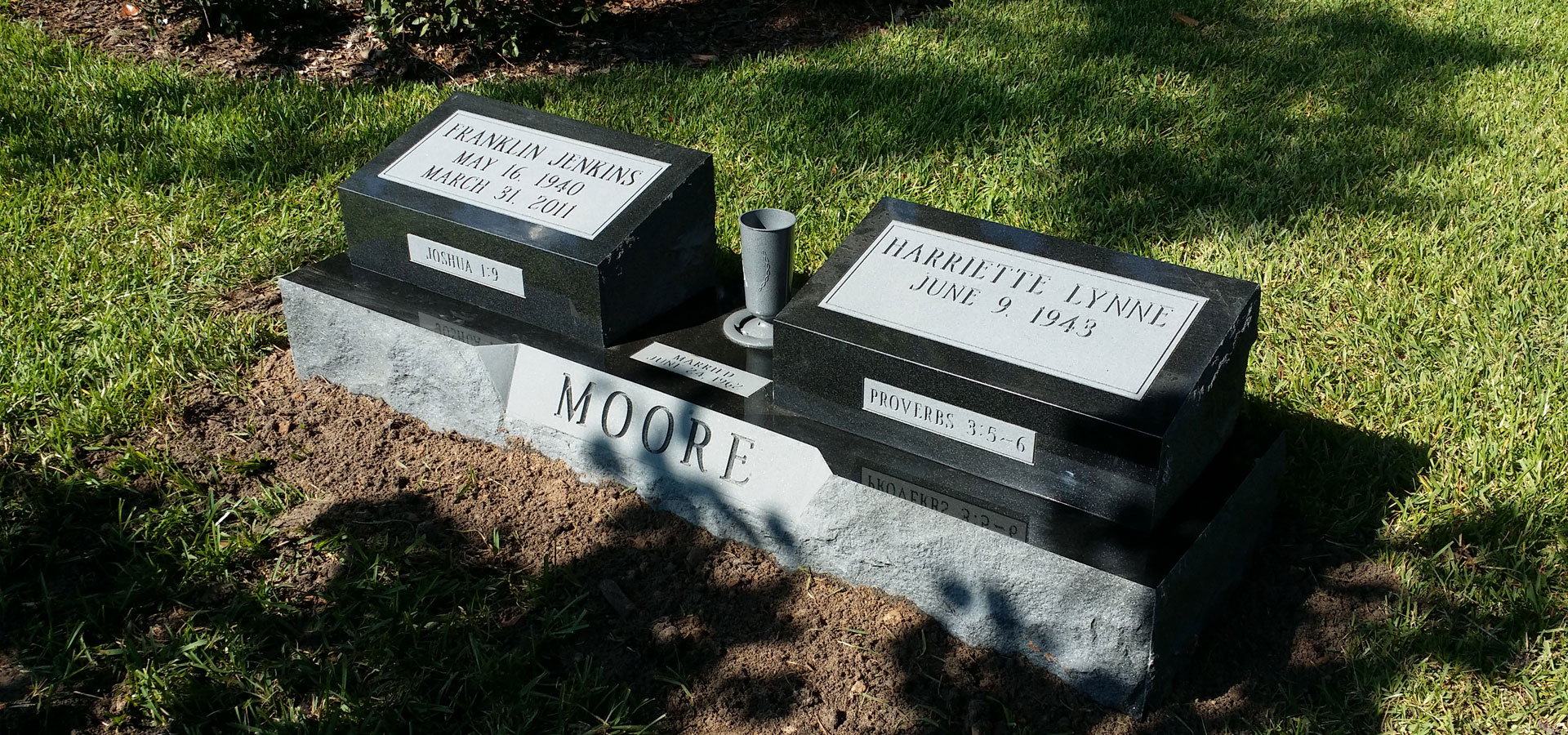Black granite double slant markers with scripture panels on a rock pitched grey base