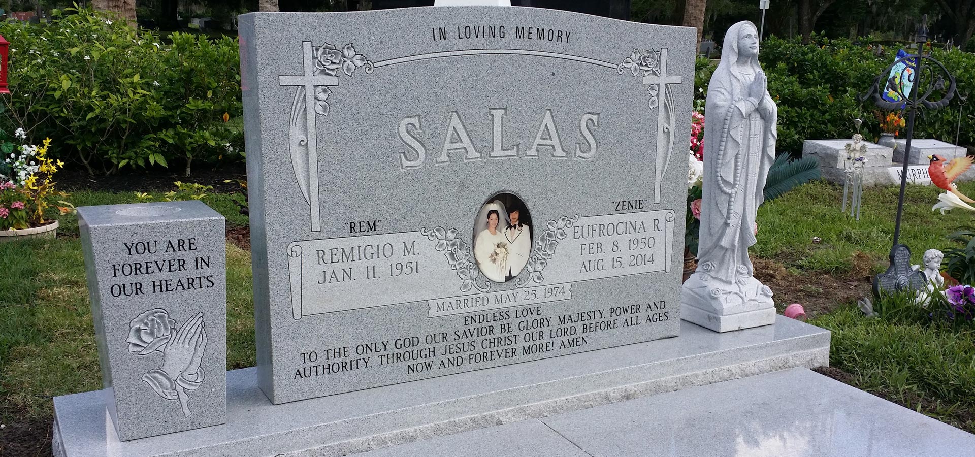 Grey granite upright with carved crosses and roses, an oval wedding portrait and a long inscription, with a carved praying hands block beside it
