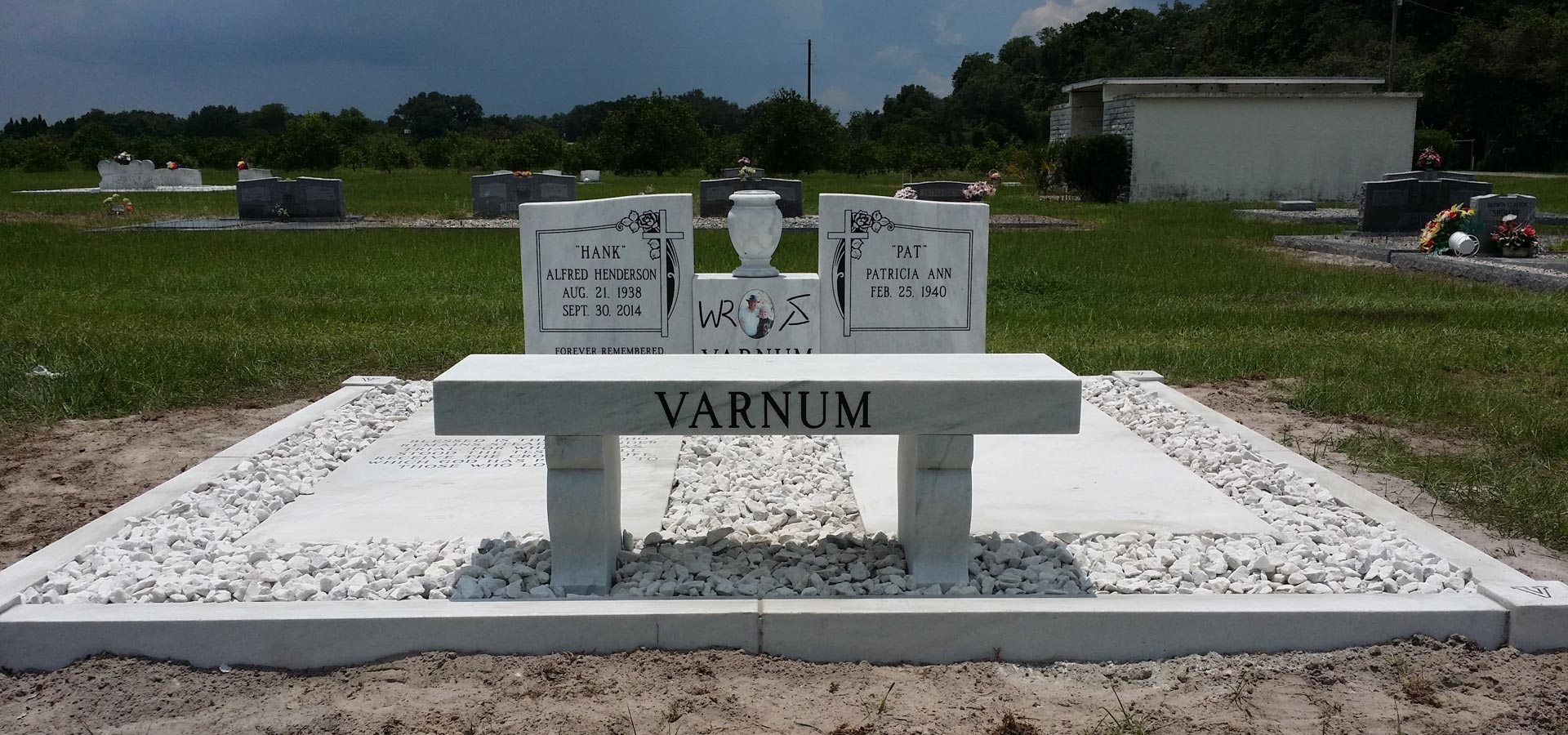White marble memorial bench in front of a double upright with a vase, on a white marble slab